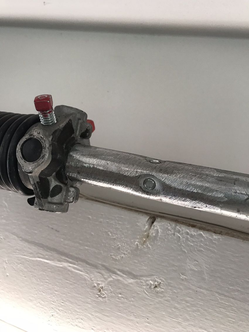Close-up of a damaged metal pipe clamp with red screw on a white wall