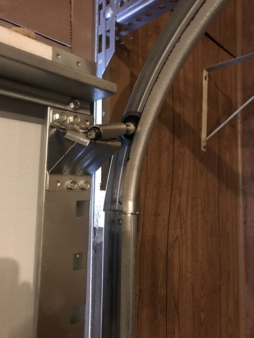 Close-up of a metal garage door hinge and curved track beside a wooden wall.