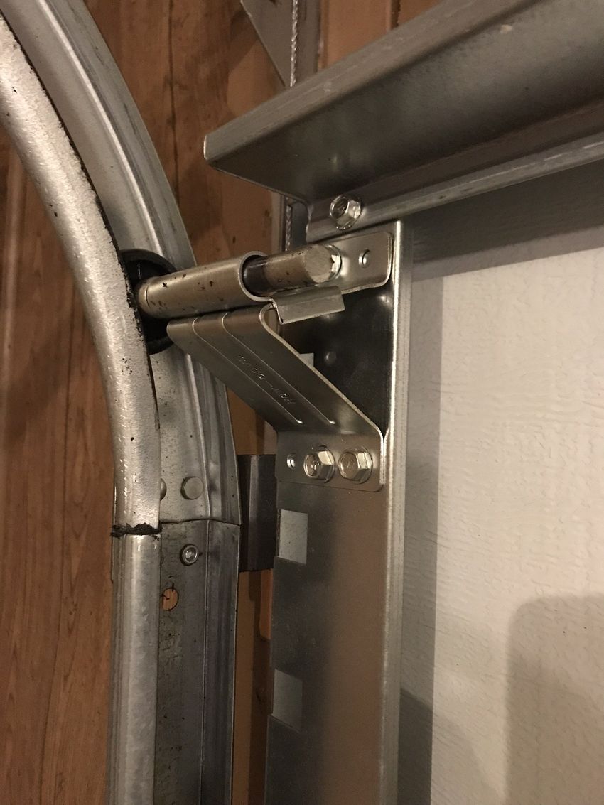 Close-up of a metal garage door hinge and support bracket against a wooden wall.