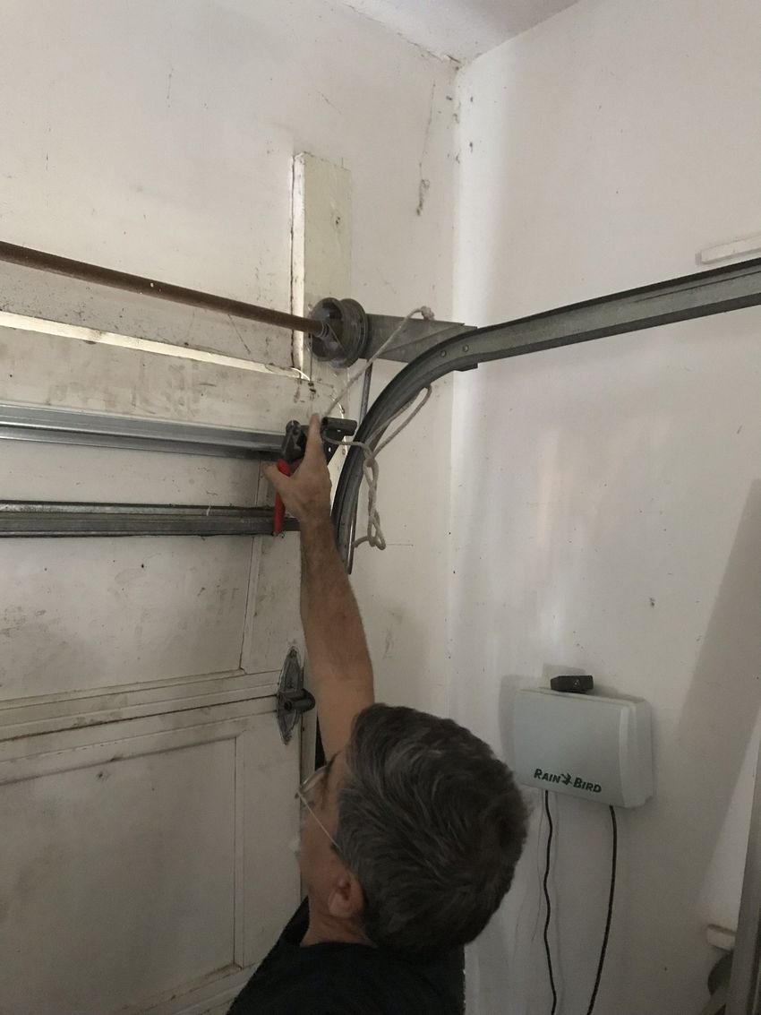 Man reaching up to inspect metal pipes and a valve on a wall near the ceiling