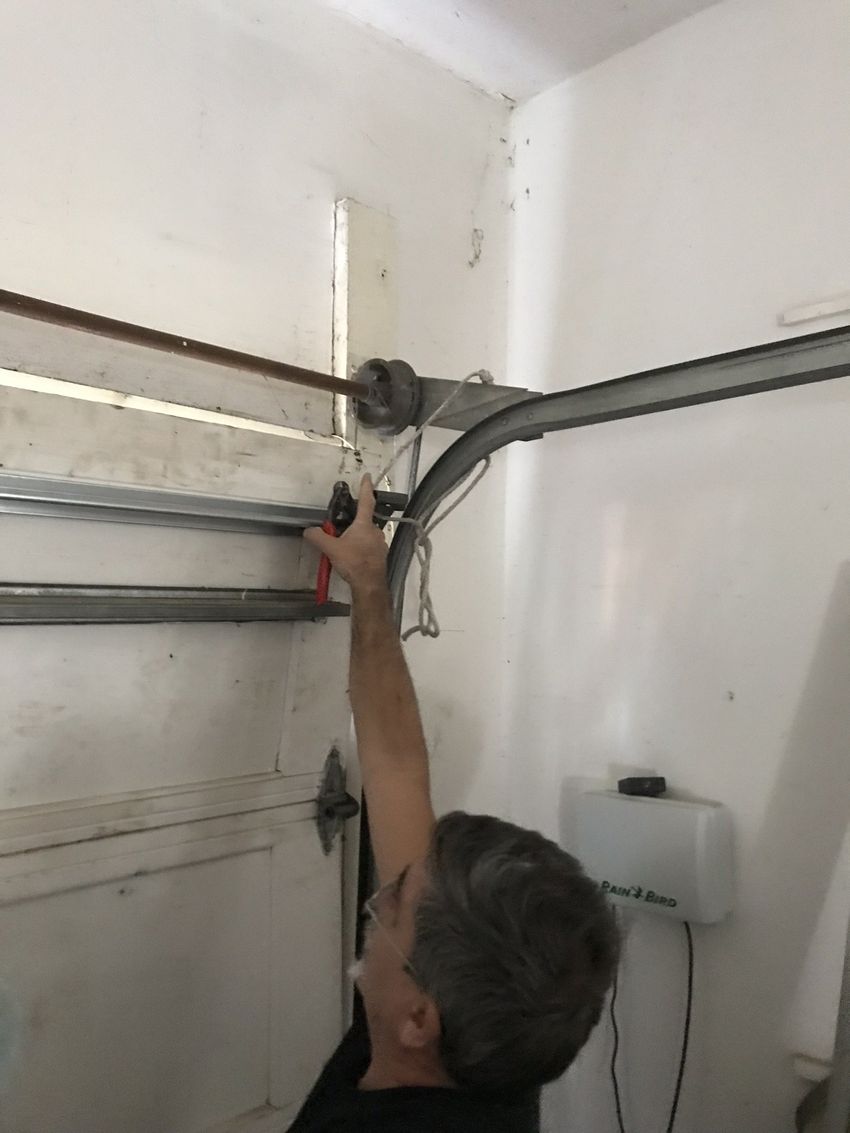 Person reaching up to adjust a garage door mechanism near the ceiling.