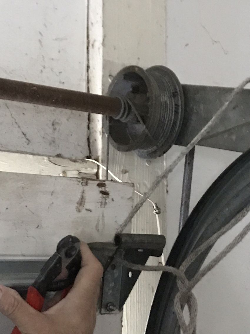 Hand holding a red-and-black tool near a cable and metal bracket on a wall
