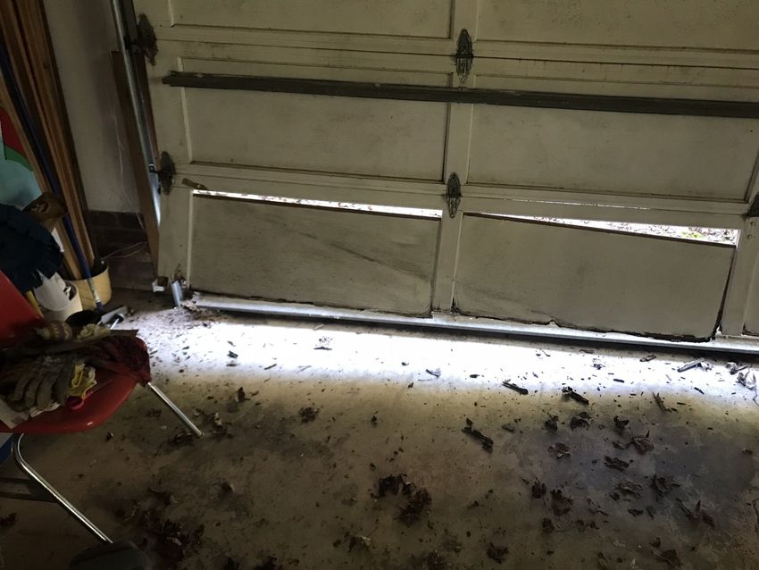 Dim garage interior with a closed white door and light spilling across a dirty floor