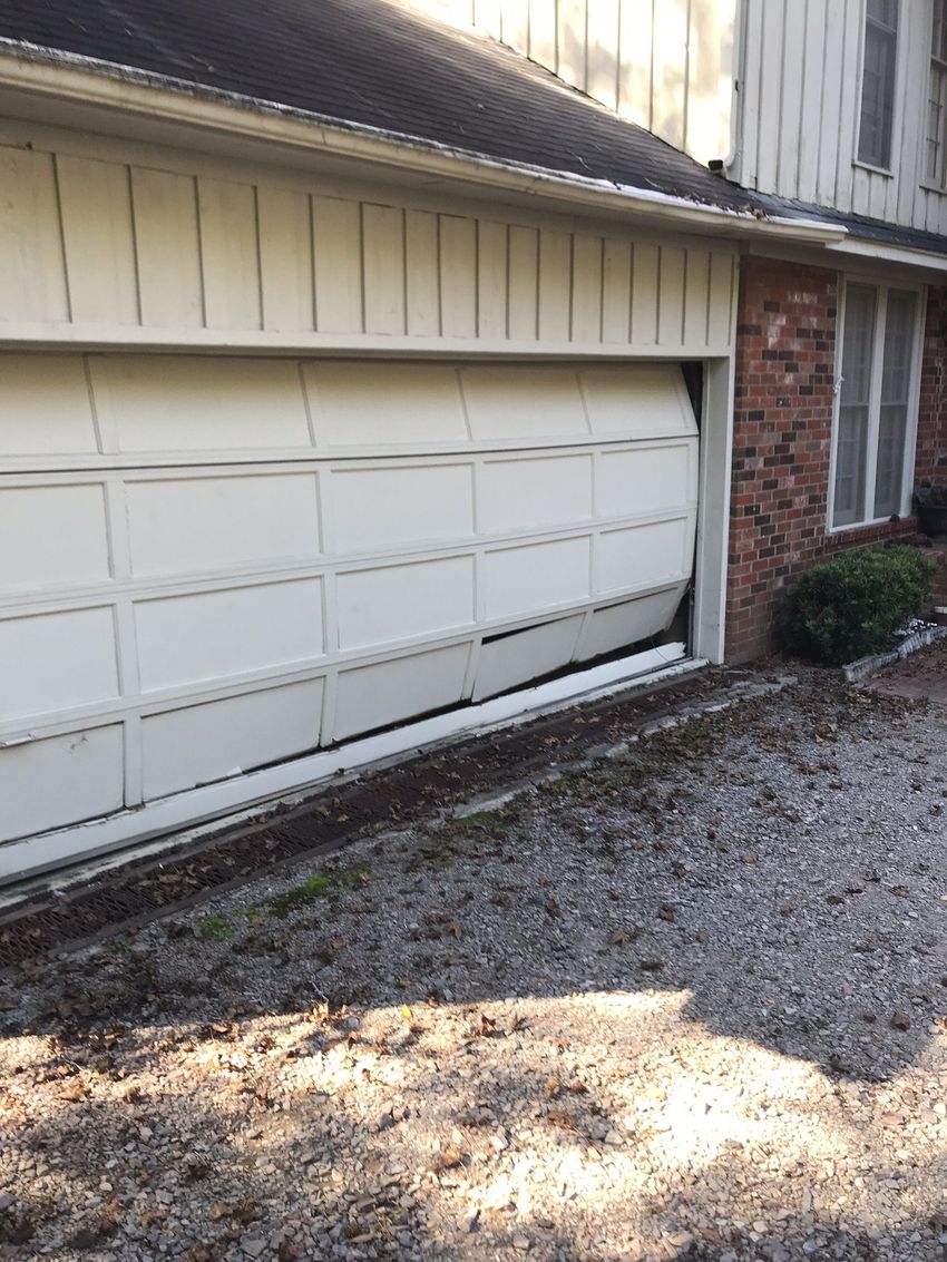 White garage door beside a brick house, viewed from a gravel driveway under a sloped roofline