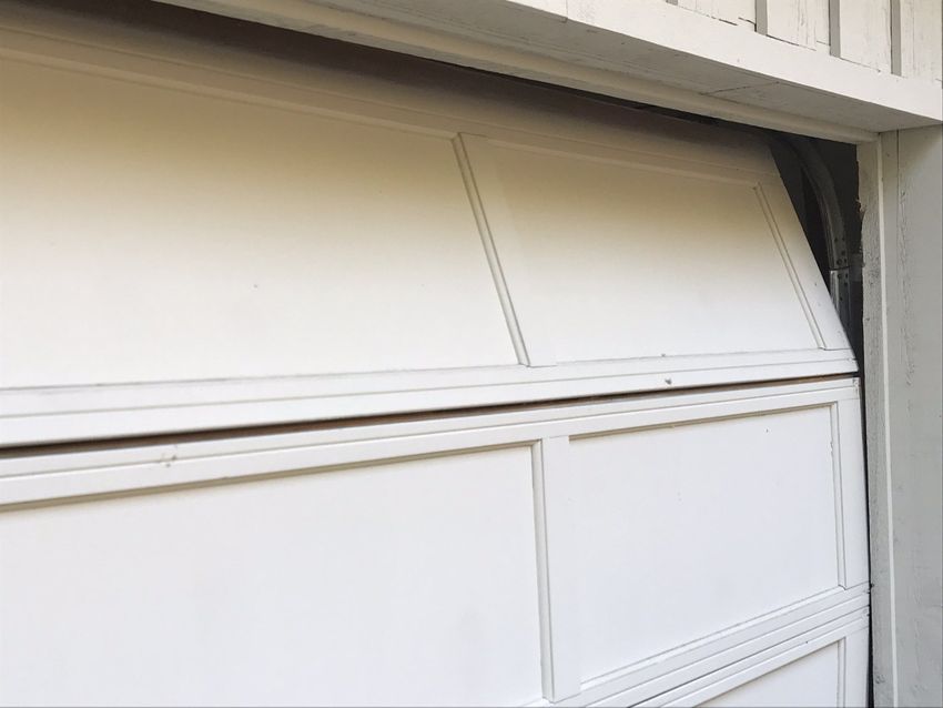 White garage door with a bent upper panel under a dark overhang