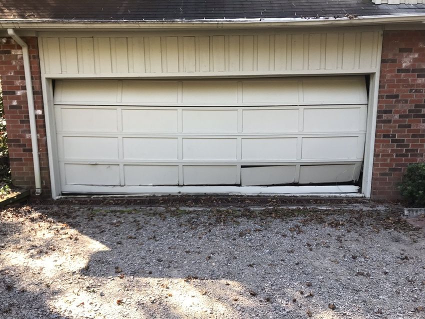 Closed white garage door with a gravel driveway in front of a brick house