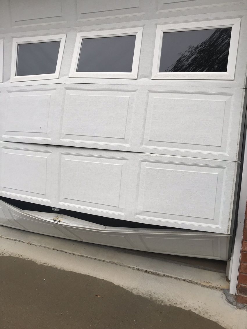 White garage door bent outward at the bottom, with three windows at the top.