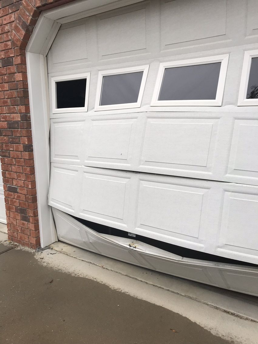 Partially damaged white garage door bent outward on a brick house