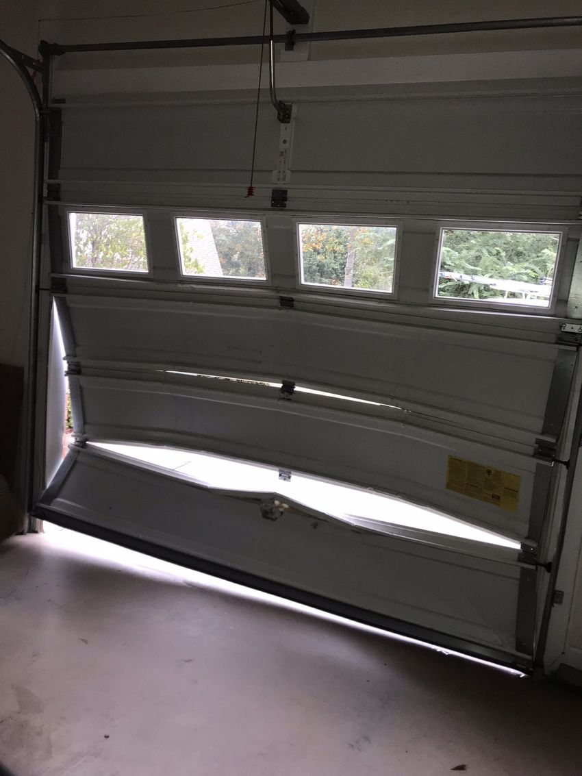 Partially open white garage door with windows, letting daylight into a garage