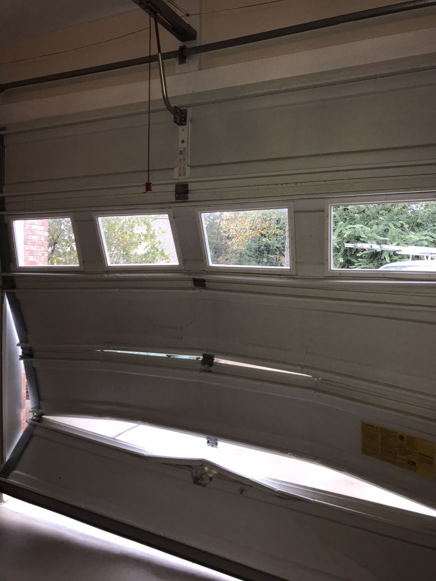 Garage door partially open with small windows and sunlight streaming in.