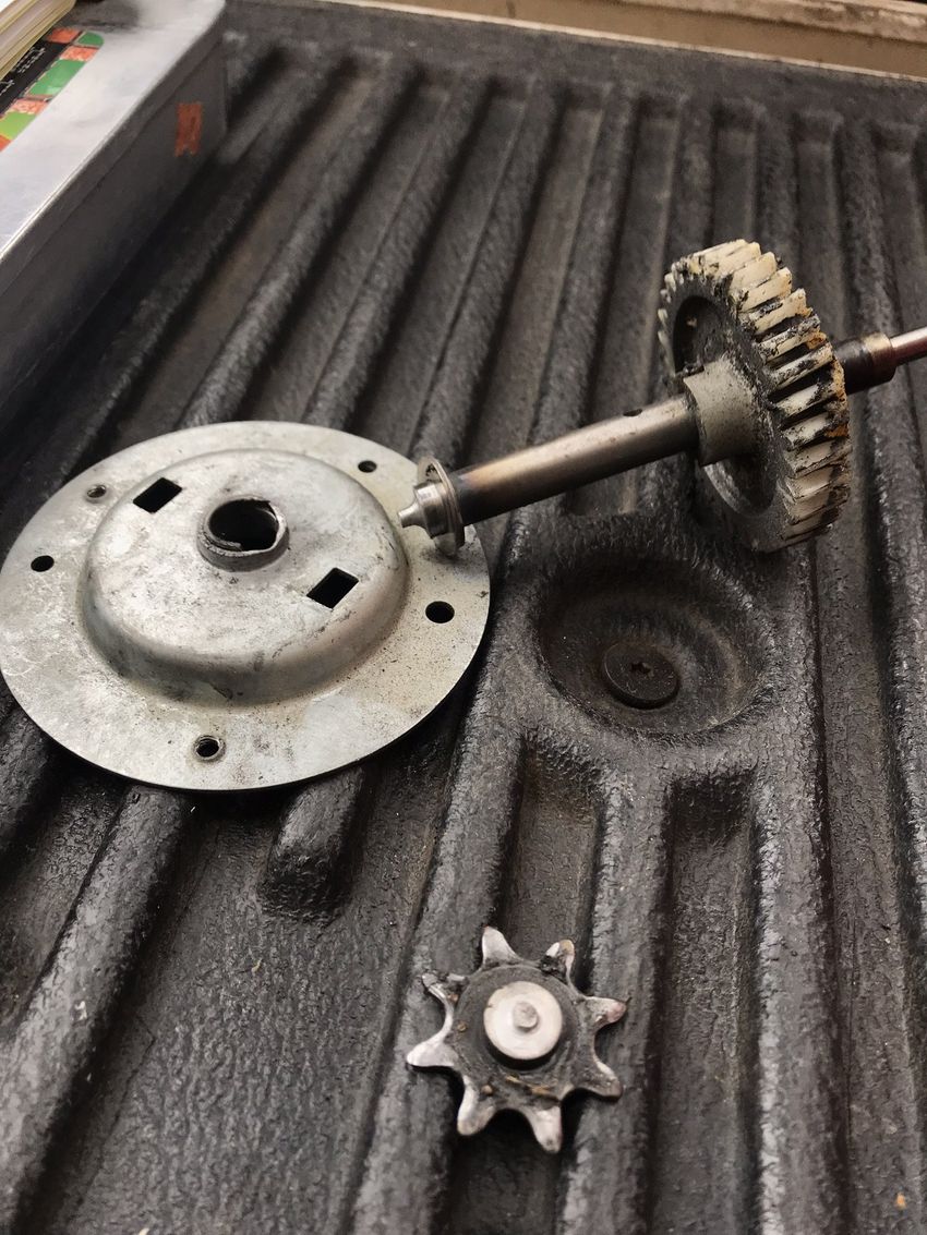 Disassembled metal parts and a small gear on a black ridged surface, likely machinery components.
