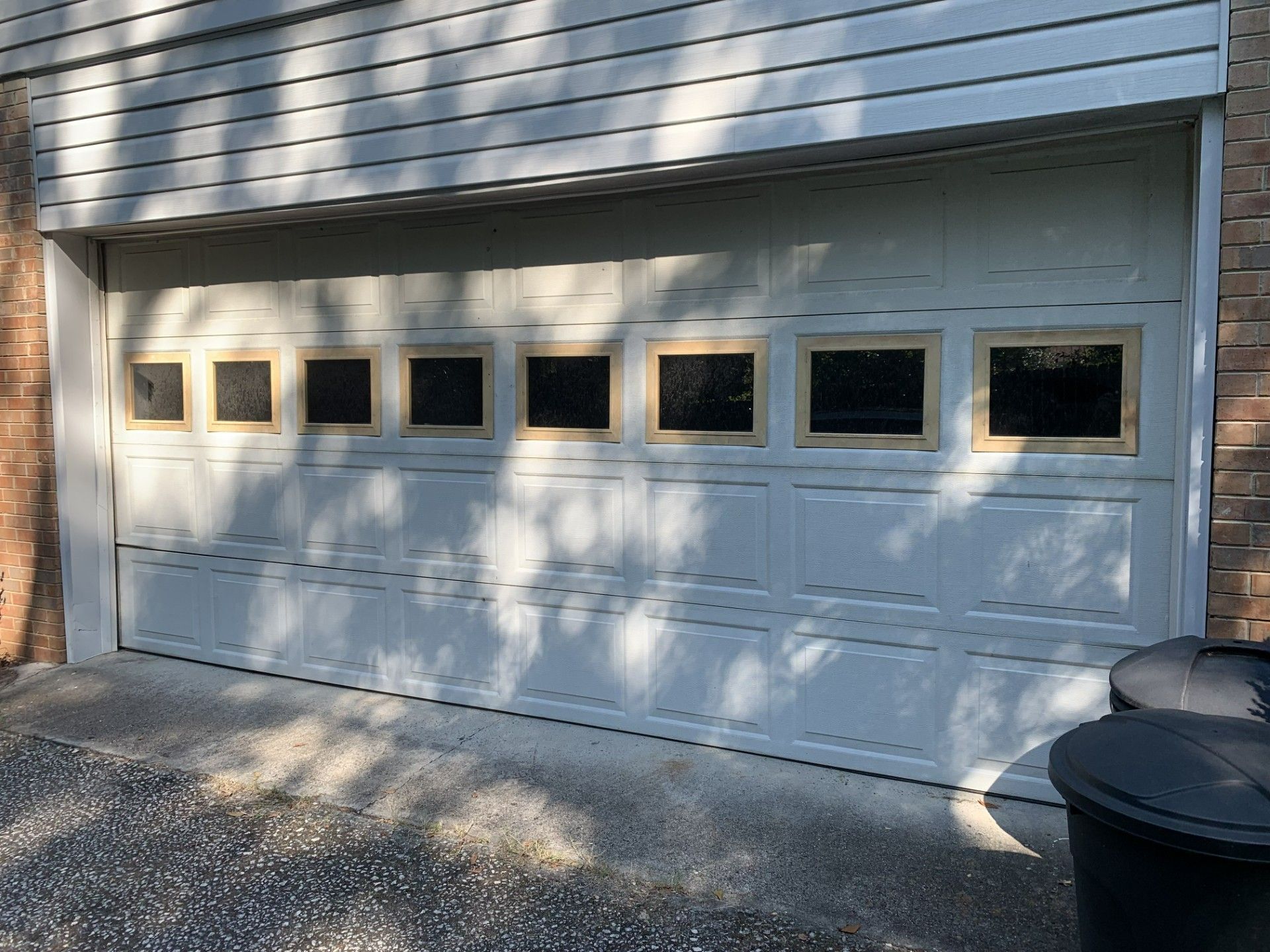 A white garage door with a lot of windows and a black trash can in front of it.