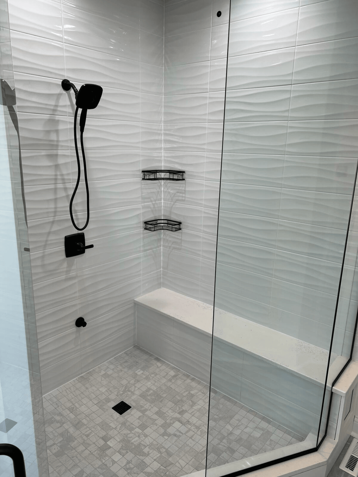 A bathroom with a walk in shower with a glass door and a bench.