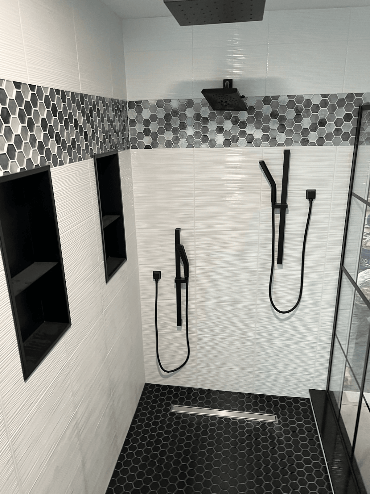 A bathroom with two shower heads and a black tile floor.