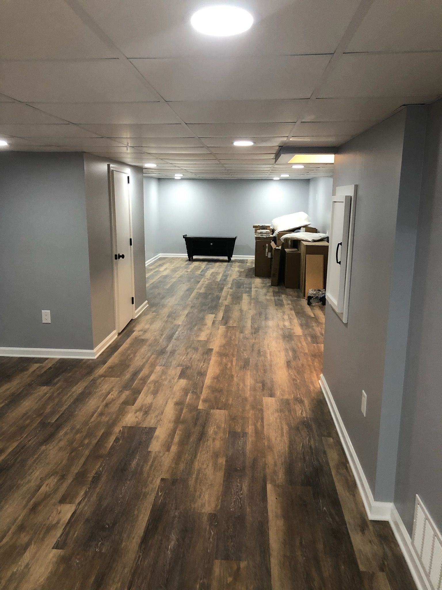A hallway in a basement with wooden floors and a pool table.