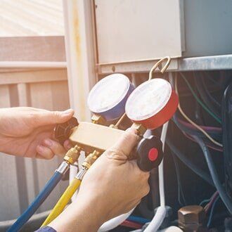 Hands connecting gauges to an air conditioning unit. Blue and red gauges attached with yellow and blue hoses in an outdoor setting.