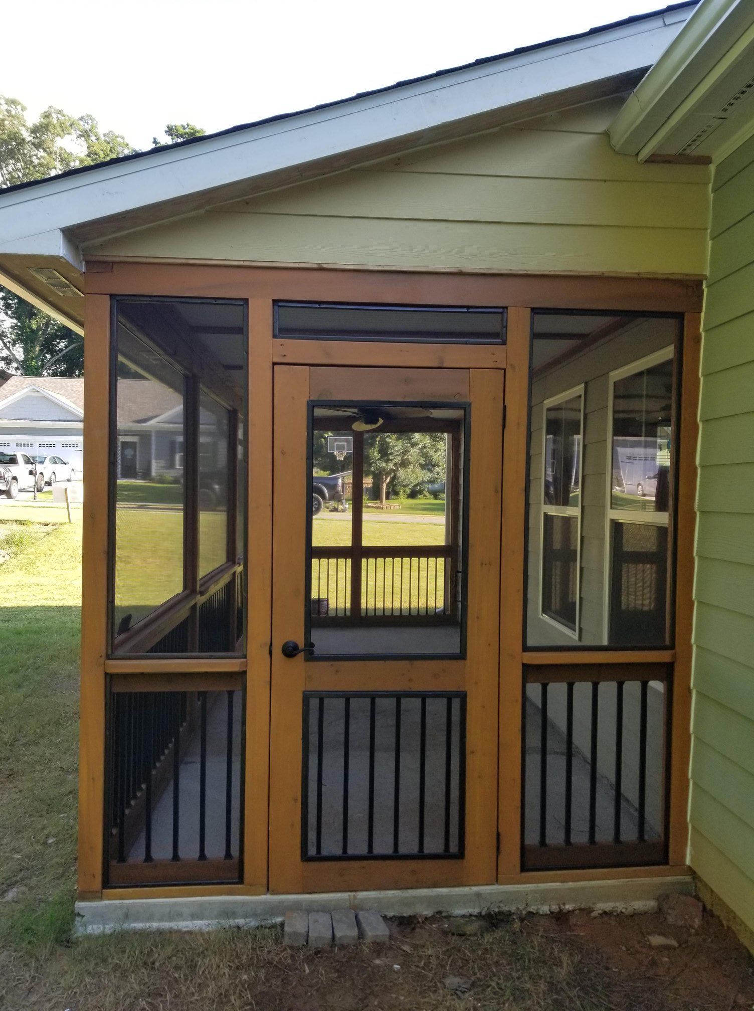 A wooden screened-in porch entrance with a central screen door and black vertical balusters, attached to a house.