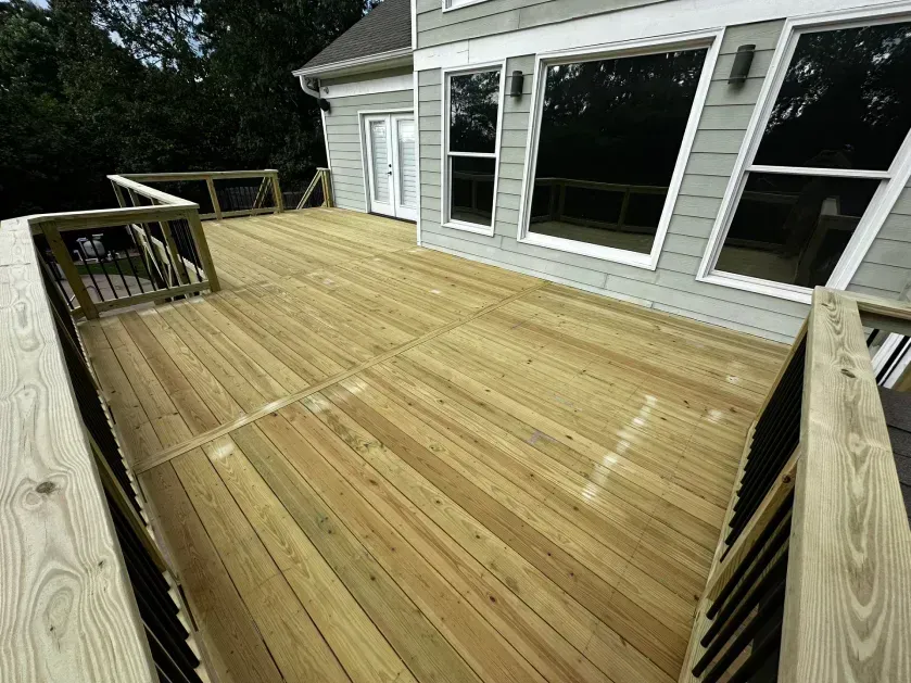 A newly built wooden deck with railings attached to the back of a light-gray house with large windows.