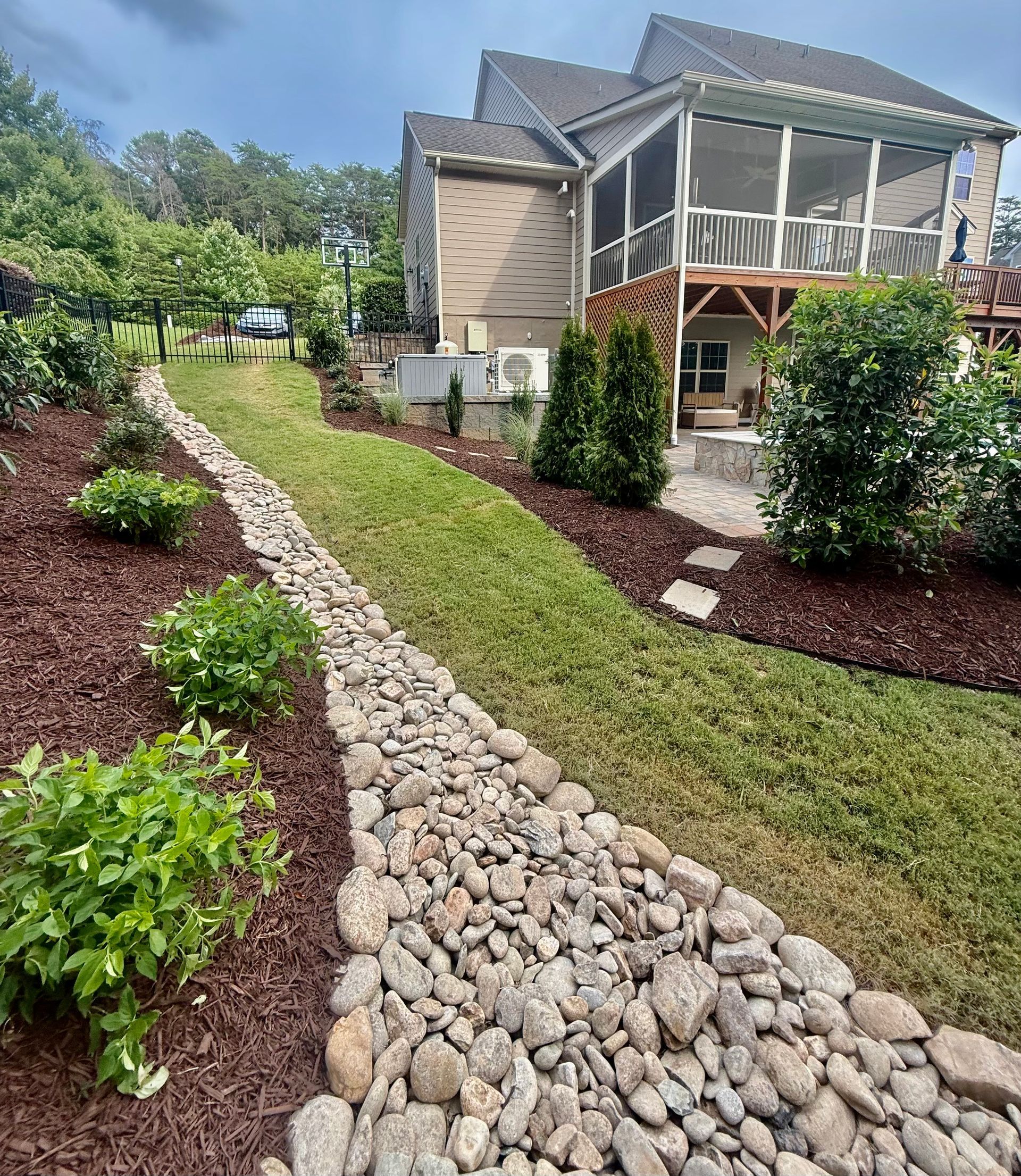 A person spreading mulch in a garden bed next to a light blue house.