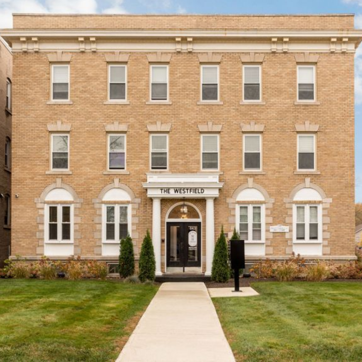 Beige brick apartment building with many windows and two entryways under a blue sky.