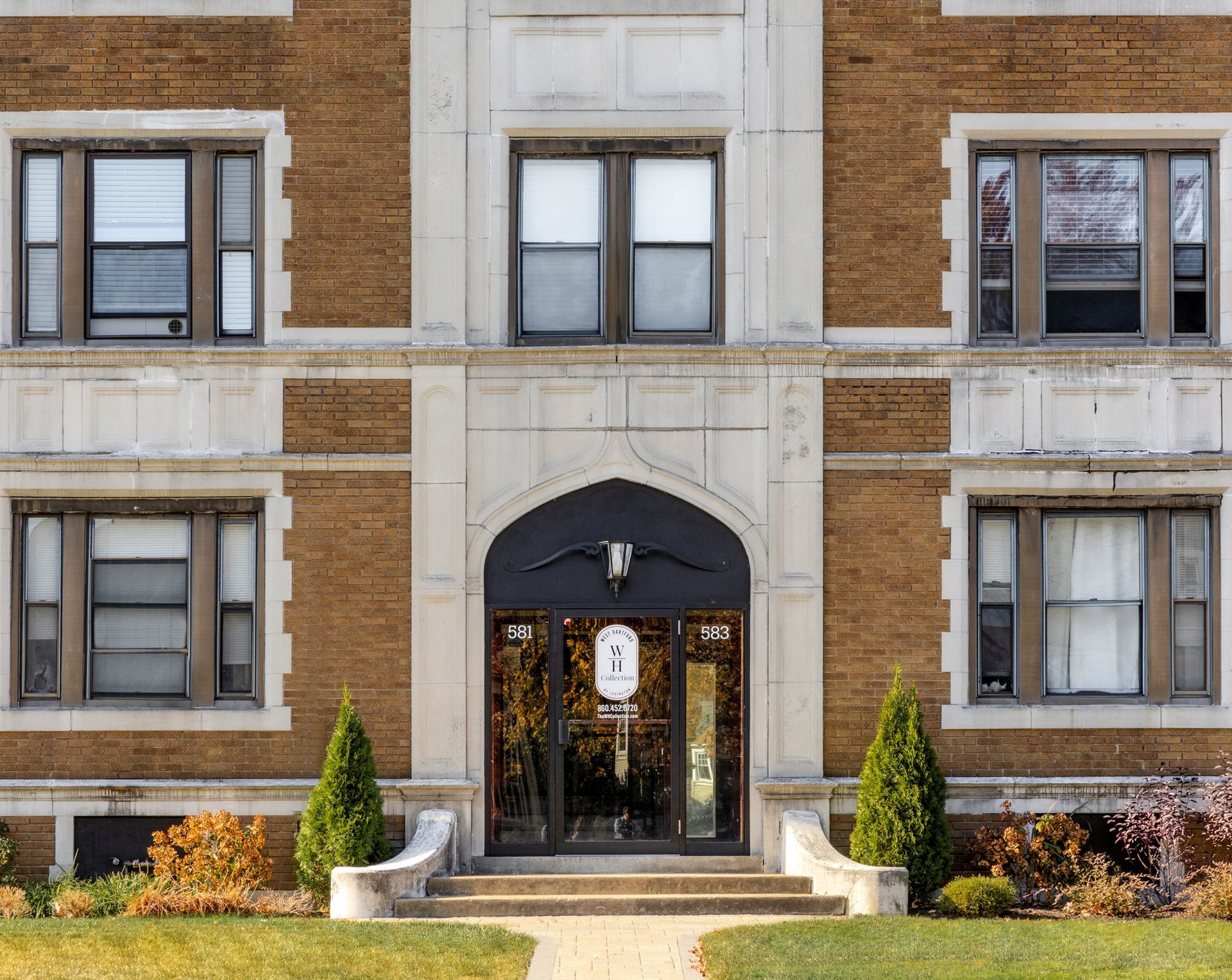 Brick building with arched doorway and multiple windows, framed by white stone.