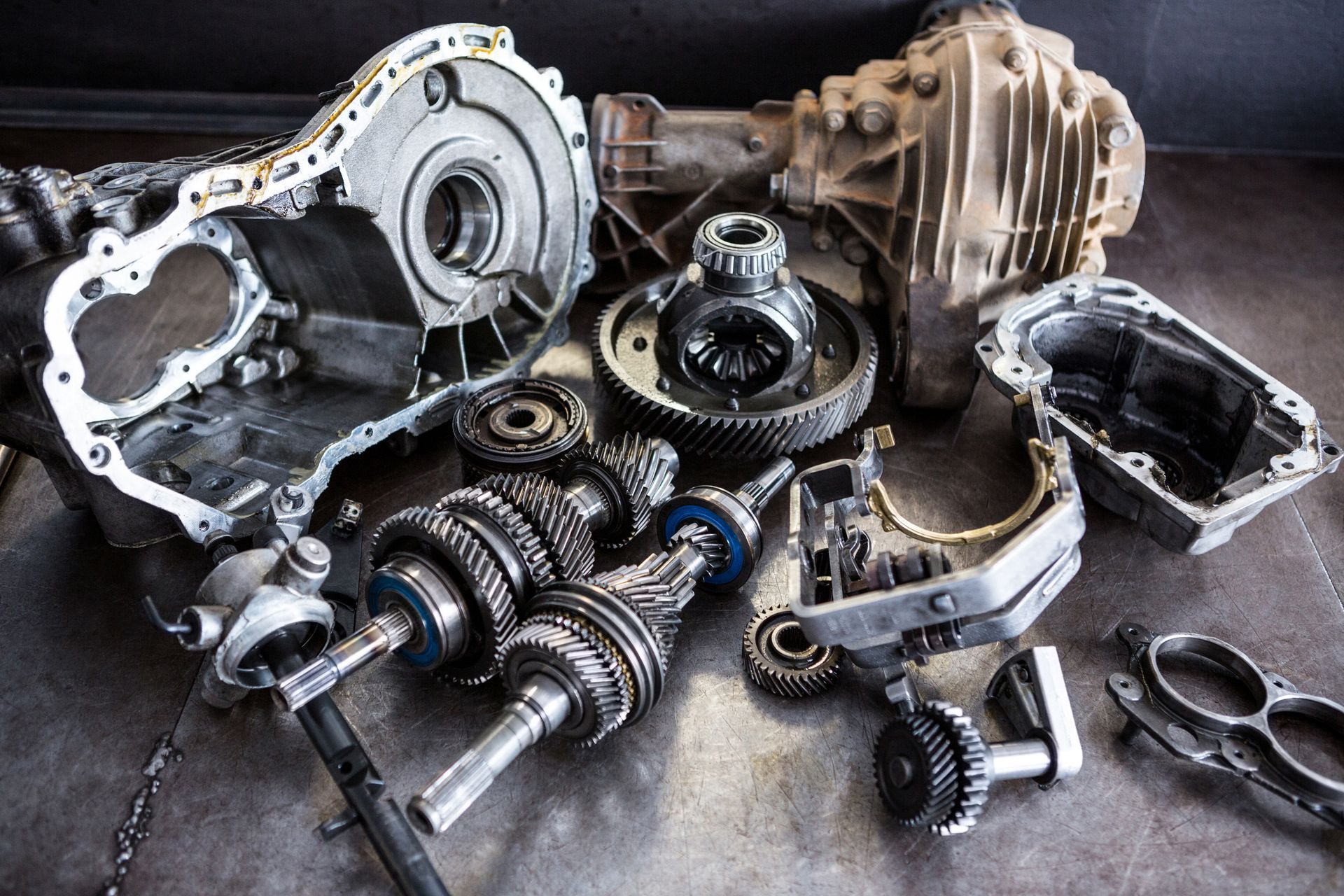 Piezas de transmisión de automóvil desmontadas sobre una superficie gris, incluidos engranajes, carcasas y ejes.