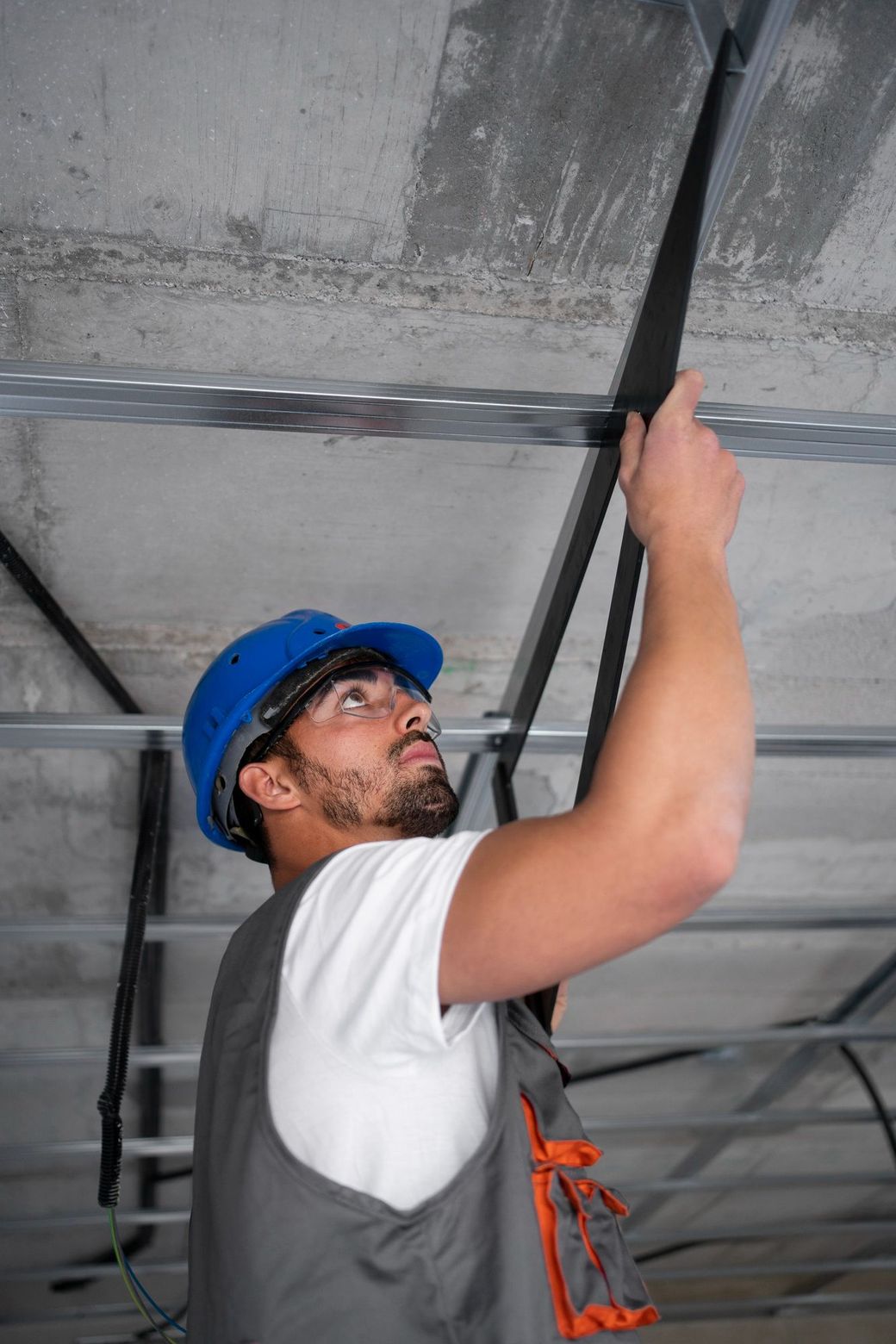Construction worker in blue hard hat installs conduit on ceiling.