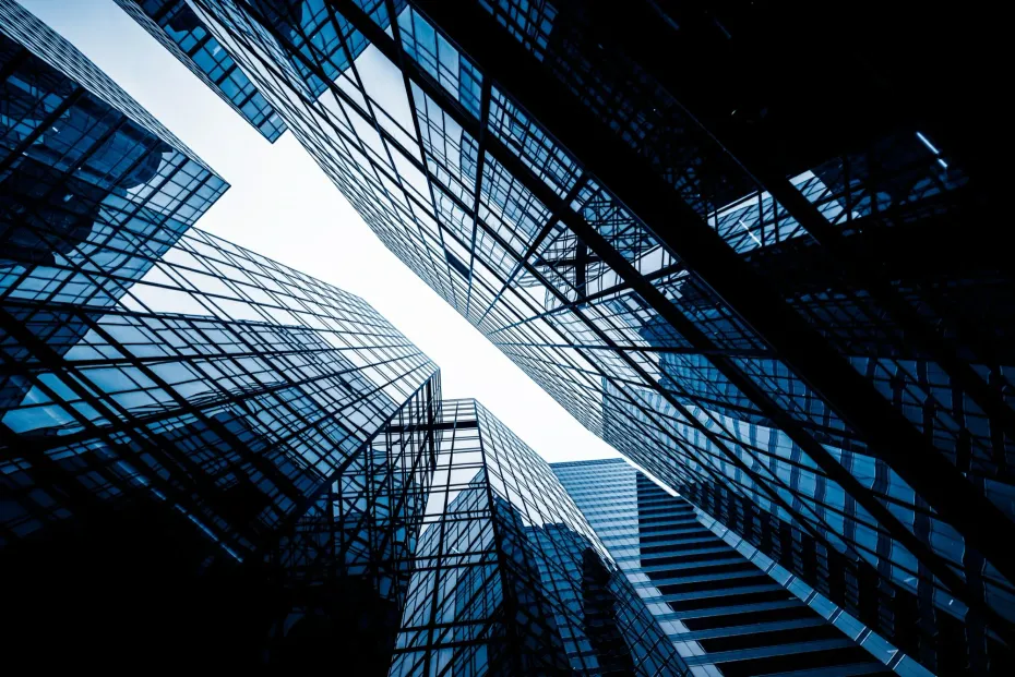 Low-angle view of modern glass skyscrapers, blue-toned, looking upward towards the sky.