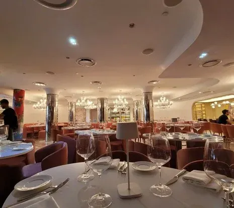 Upscale restaurant interior with round tables, chairs, and multiple chandeliers.