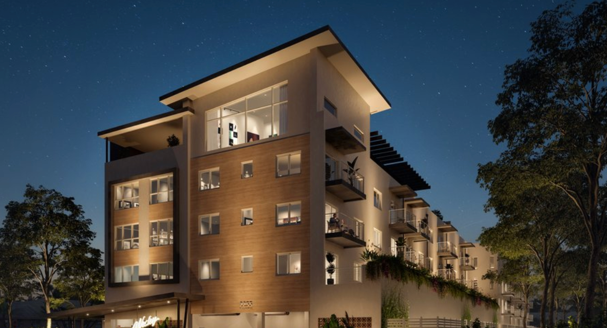 A modern four-story apartment building with tan siding and lit balconies at night under a starry sky.