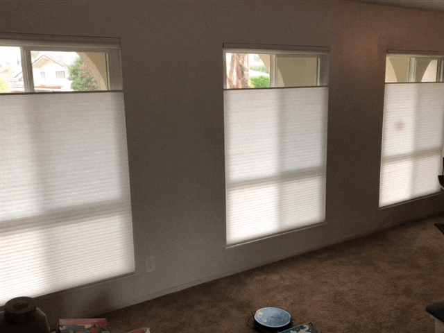 A living room with three windows and white blinds on them.