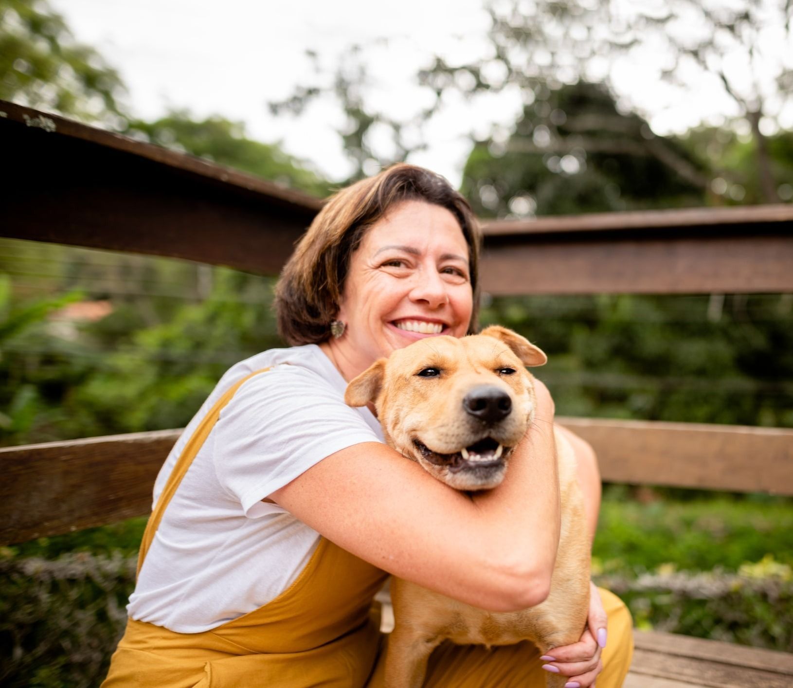 A woman is sitting on a bench hugging a dog.