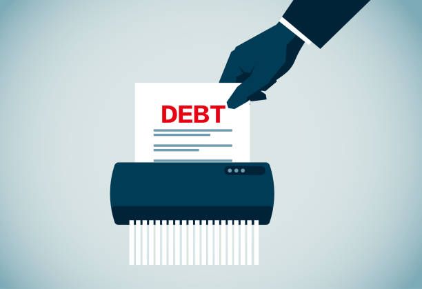 a hand is shredding a piece of paper with the word debt on it .