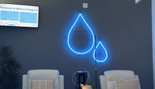 Blue neon water drop sign on a dark wall above white chairs, with a television screen.