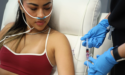 Woman receiving IV treatment with oxygen tube, in a medical setting, hands of medical personnel present.