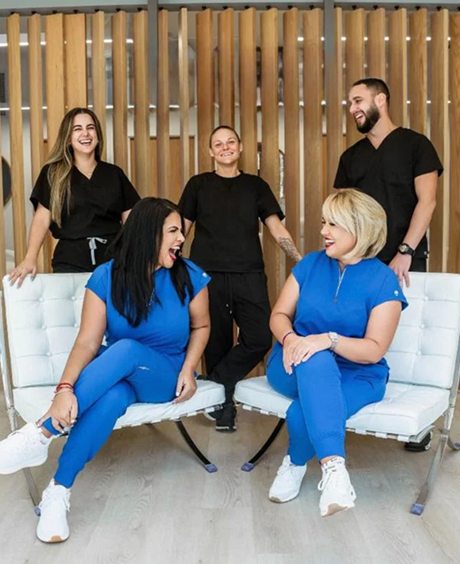 Medical professionals in blue and black scrubs pose in a modern office, smiling.