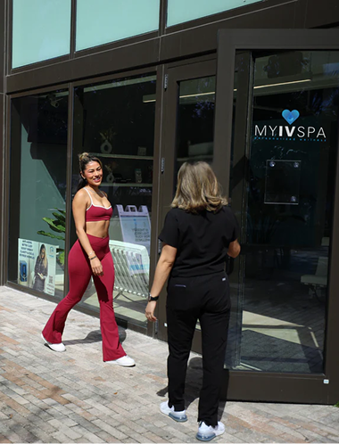 Woman in red activewear exits "MY IV SPA" with another person opening the door.
