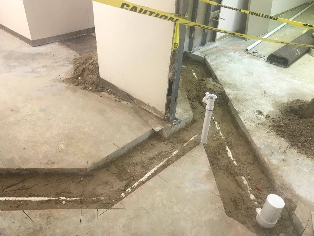 Construction site with excavated trenches, PVC pipes, and caution tape.