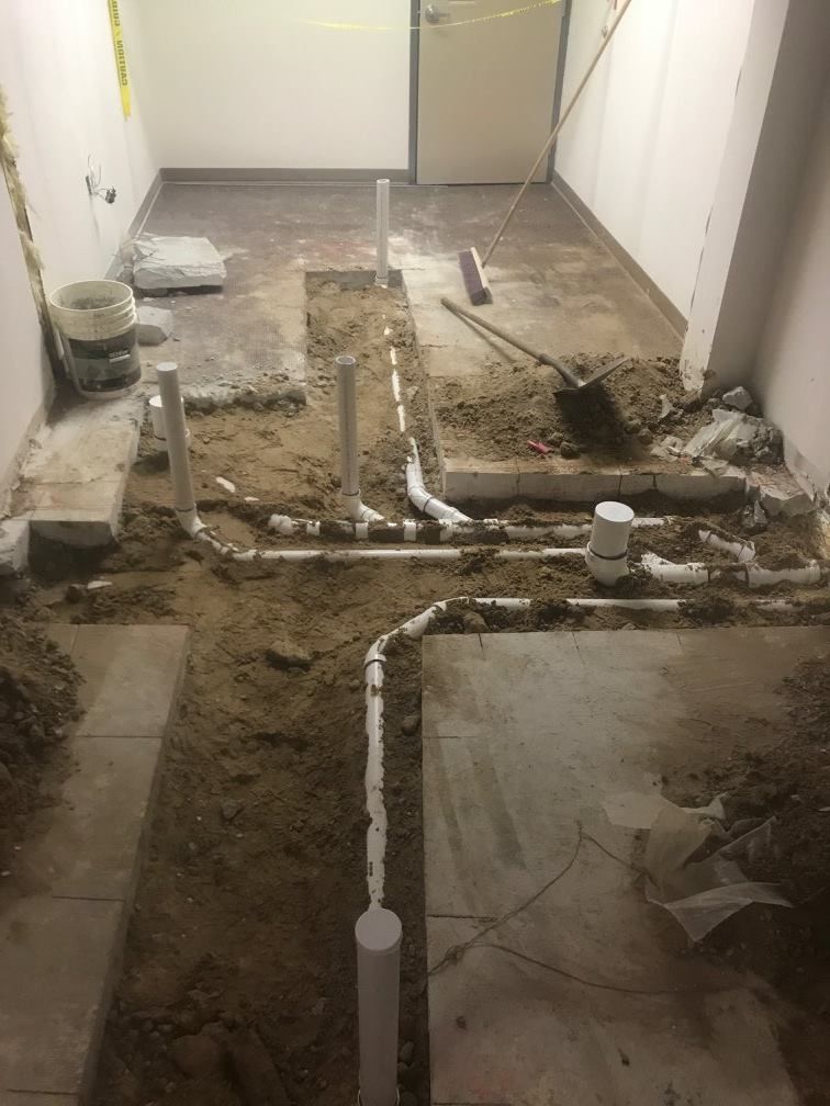 Interior view of plumbing renovation with exposed pipes in a room. Dirt and debris are visible.