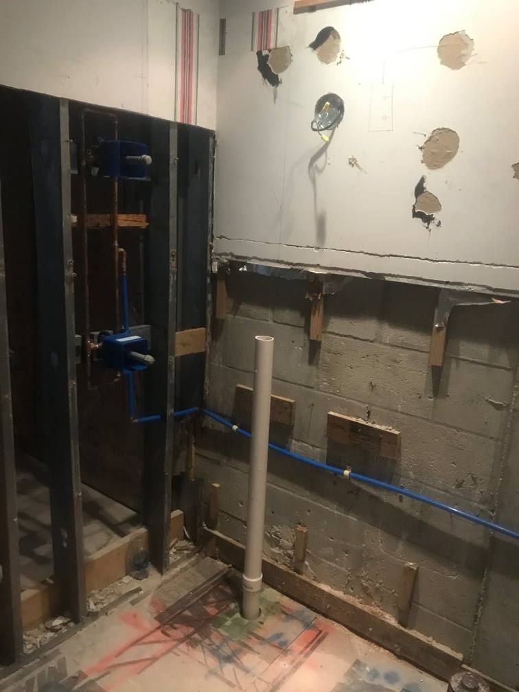 Bathroom remodel in progress; exposed studs, plumbing, and wall. White wall has holes; blue PEX pipes.