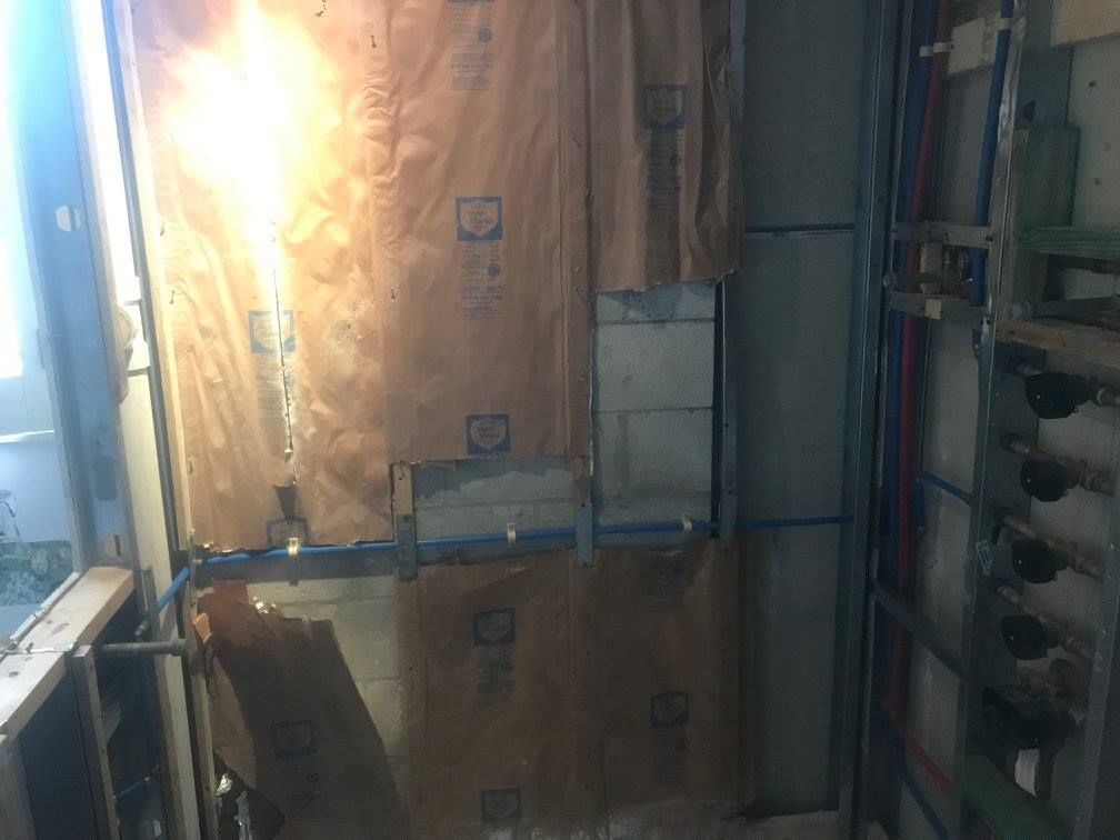Interior wall under construction, with exposed insulation, framing, and plumbing.