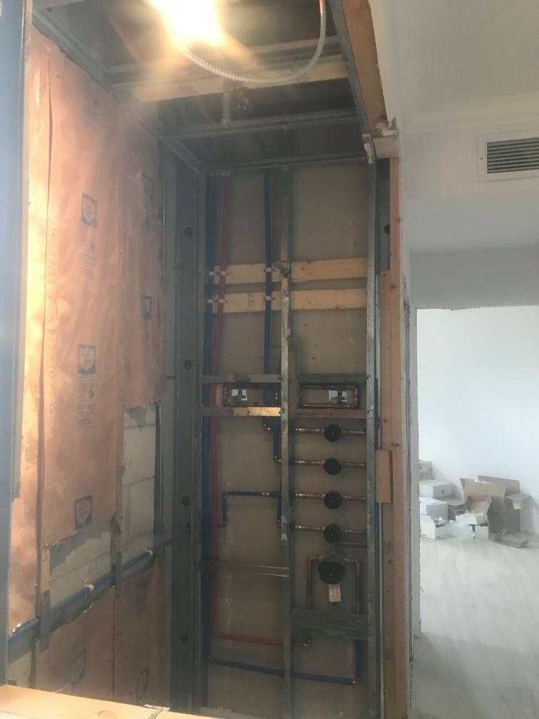 Framed, open wall with exposed plumbing and electrical components, construction site.