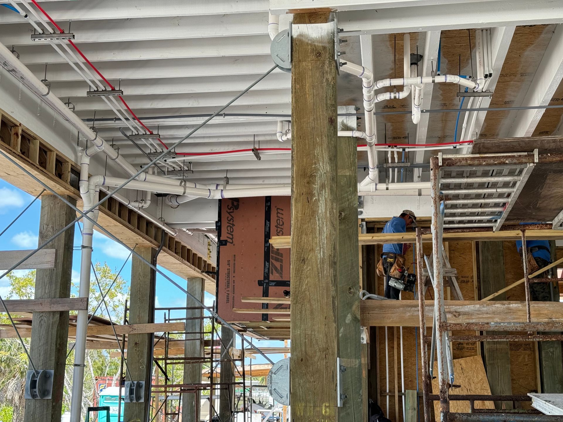 Construction site interior with scaffolding, exposed beams, and workers installing materials on an upper level