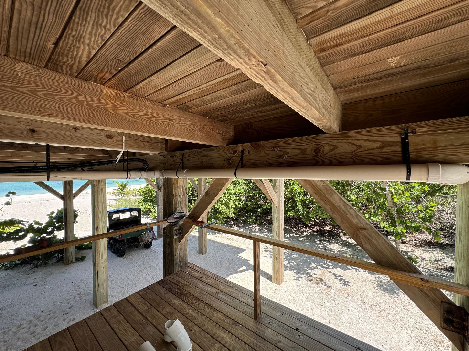 Wooden porch under construction with exposed beams, railing posts, and a view of yard and vehicles outside