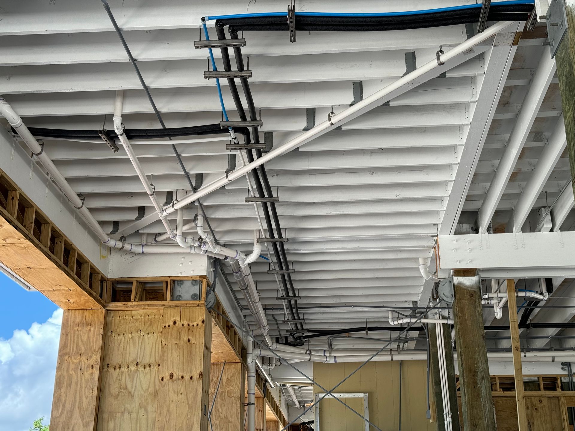 Underside of a white-painted stairway under construction with exposed beams and pipes indoors