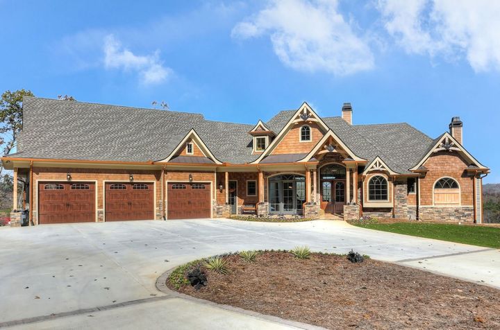 Large brick suburban house with a three-car garage and curved driveway under a blue sky