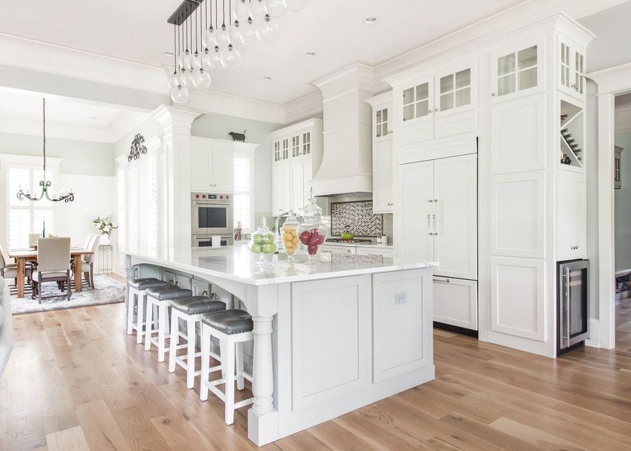 Bright white modern kitchen with a marble island, black stools, and hardwood floors