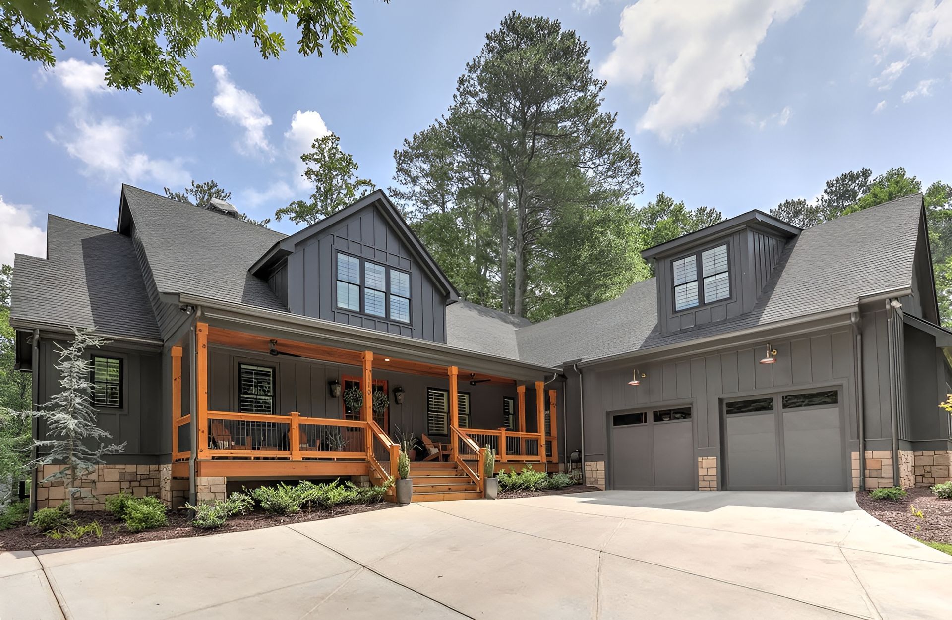 Modern gray house with orange-trim porch, twin garages, and a tree-lined driveway under a blue sky