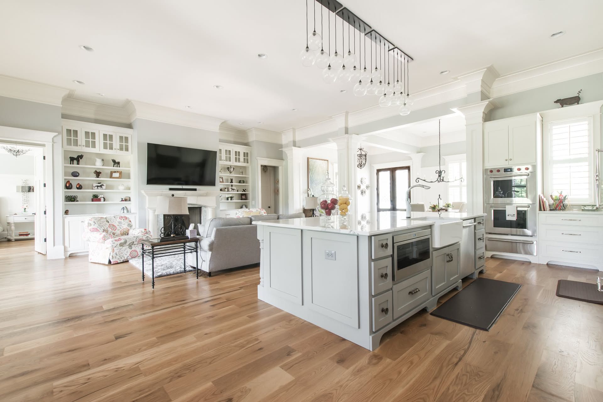 Bright modern open-plan kitchen and living room with white cabinets, island, hardwood floors, and large windows