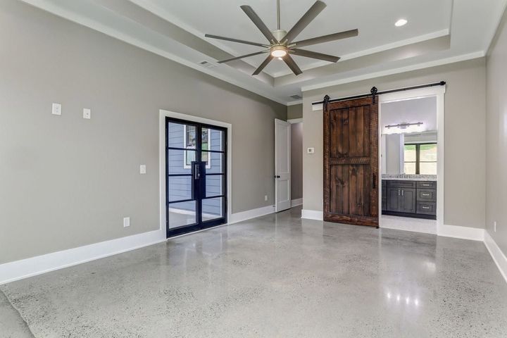 Modern empty room with glossy tile floor, gray walls, ceiling fan, and a rustic barn door.